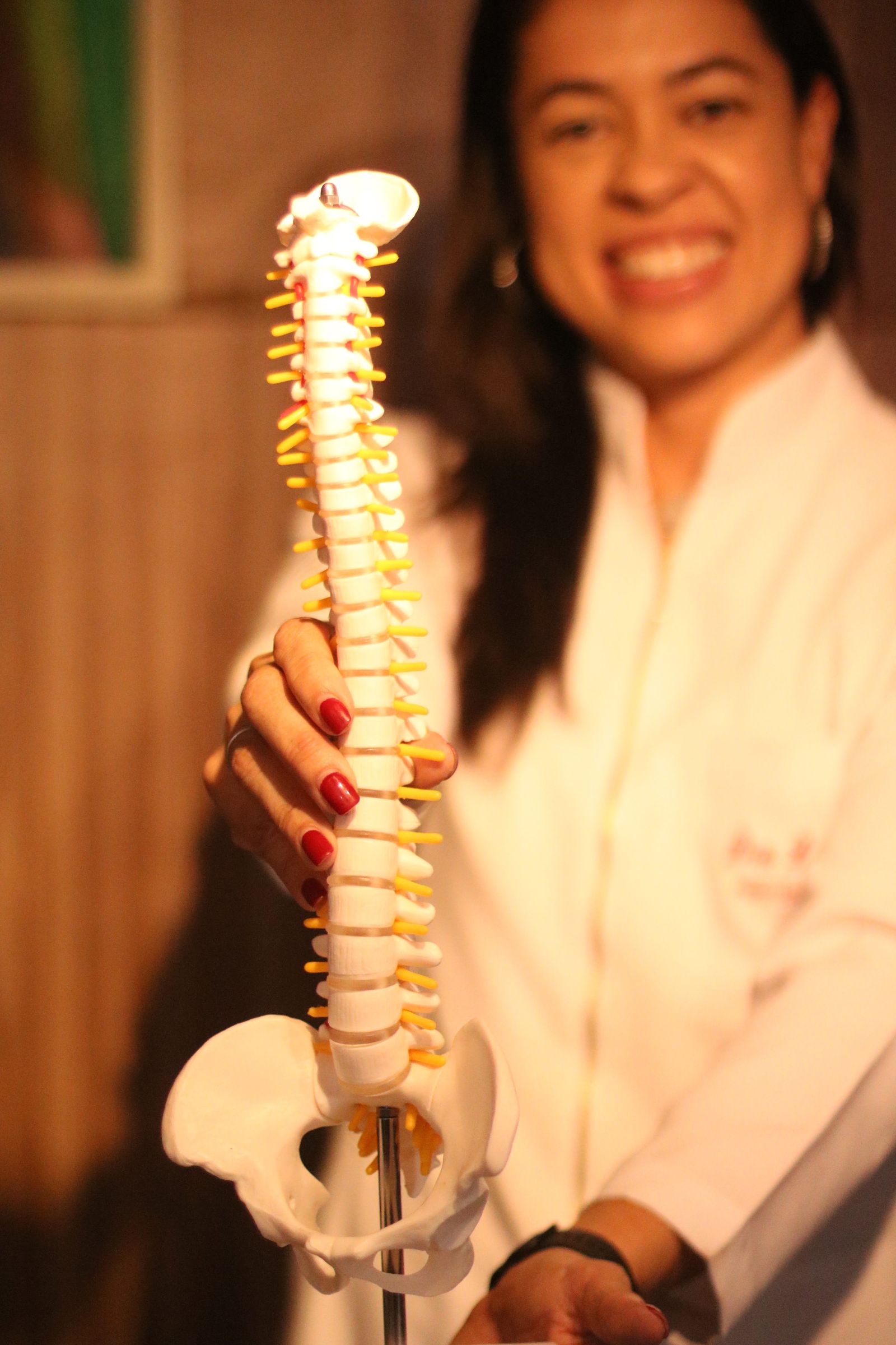 Dra. Luelma Rocha sorrindo ao lado de um modelo anatômico de coluna vertebral